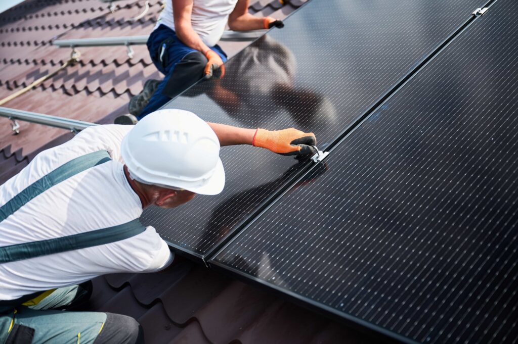 Dois homens a instalar painéis fotovoltaicos no telhado de uma casa